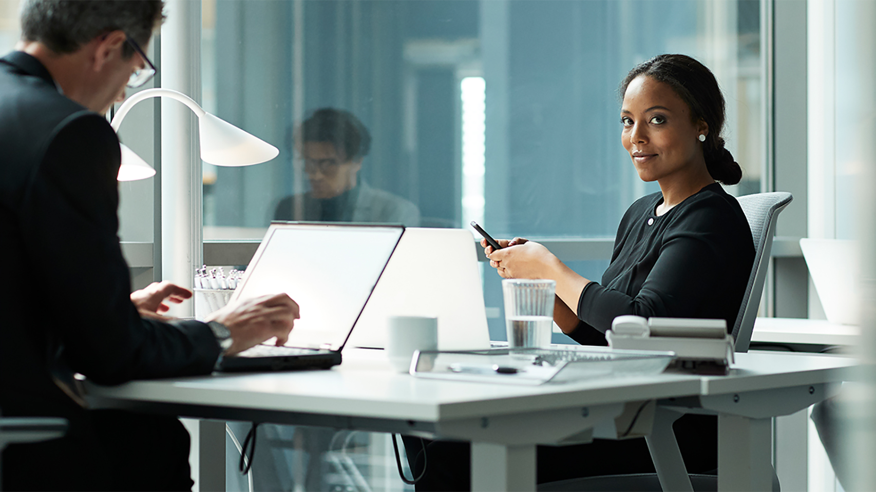 Business woman texting at a shared desk while look at the camera.