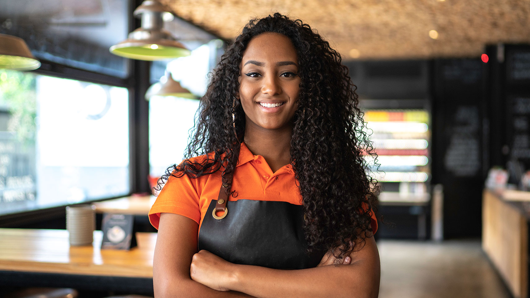 Young woman in an apron with her arms crossed, smiling at the camera