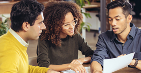 Three young adults looking at a single paper while sitting at a conference room table