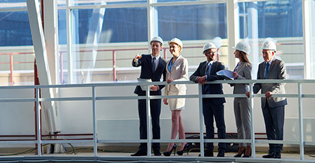 A group of businesspeople wearing hard hats and overlooking a commercial construction site