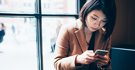 Woman looking down at her phone while sitting next to a window.