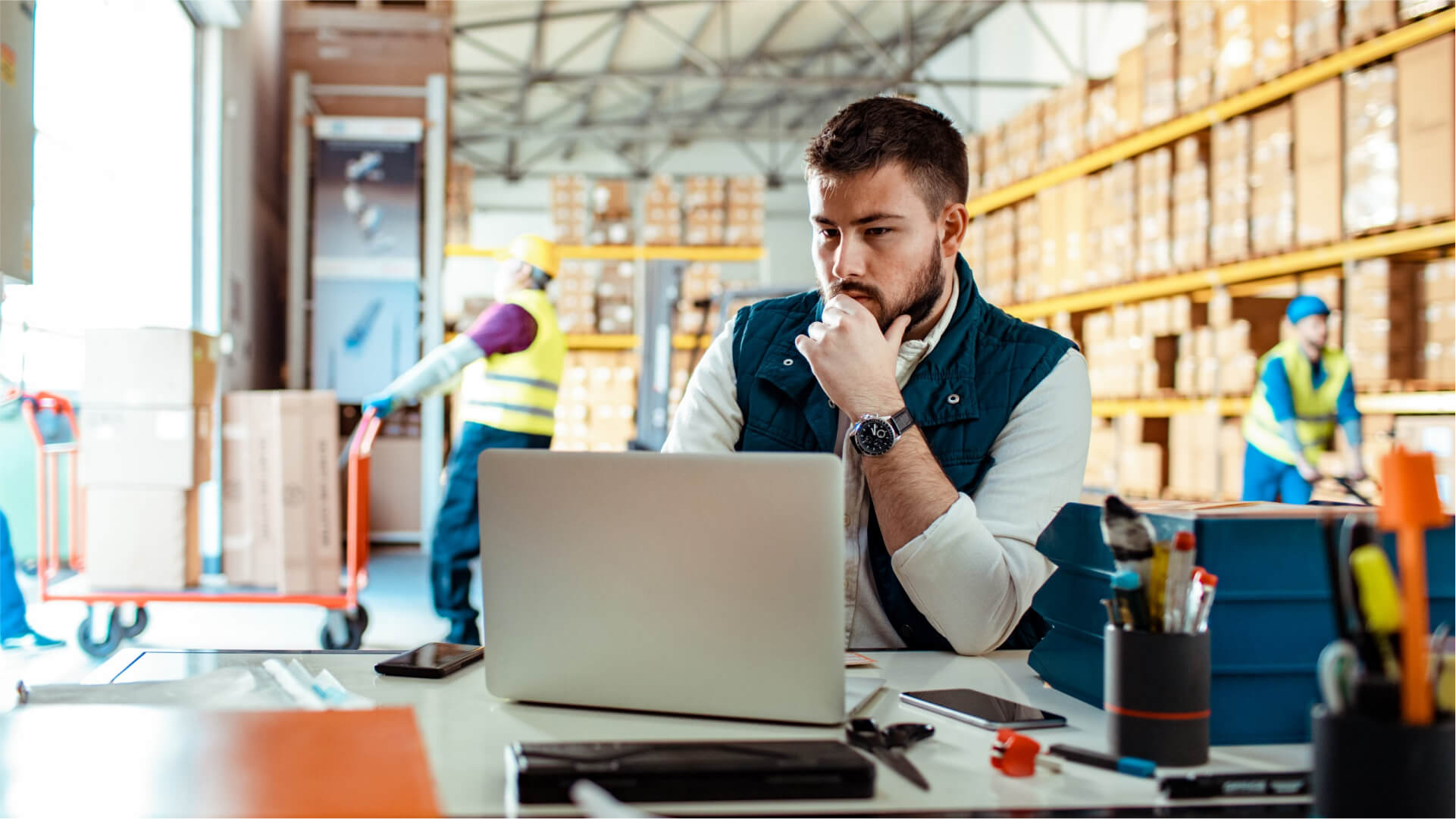 Man sitting at a desk working on a computer in a warehouse.