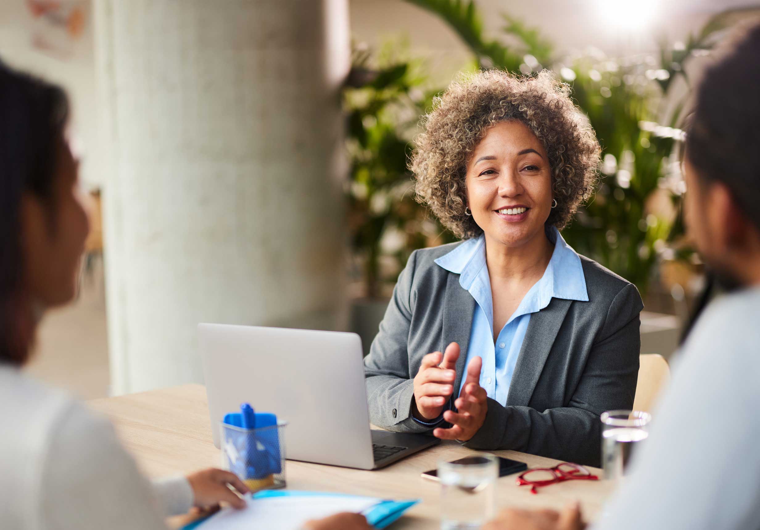 A Western Alliance Bank financial advisor with short curly hair is smiling and gesturing while seated at a table with her computer. She is meeting with a client to discuss their financial needs, symbolizing the expert and personalized service we offer.