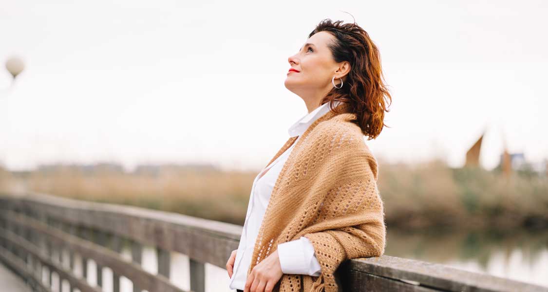 A woman on a coastal boardwalk standing in the sunlight 