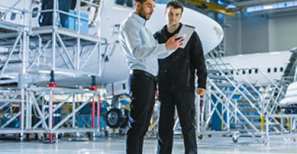 Two men in an air hanger looking at a tablet computer