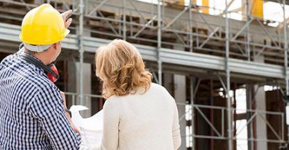 Two people at an industrial construction site looking at plans and the building