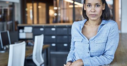 Business woman in office leaning on a table looking into the camera