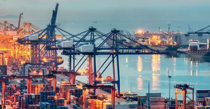 Picture of an industrial port at night with a cargo ship in the water.