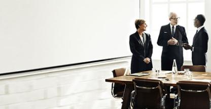 A group of three business people standing and speaking in a boardroom