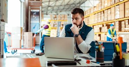 Man sitting at a desk working on a computer in a warehouse.