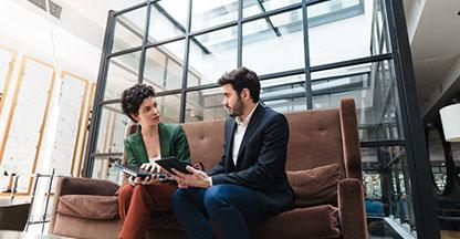 Man and woman sitting on couch looking at an tablet computer. 