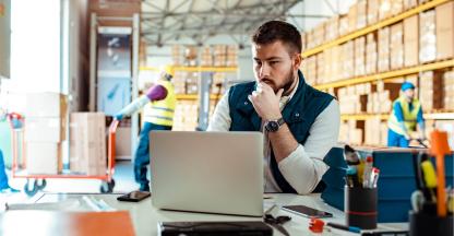 Man sitting at a desk working on a computer in a warehouse.