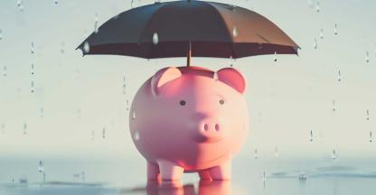 A piggybank with an umbrella staying dry in the rain