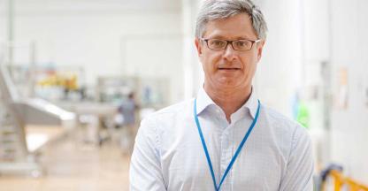 A manufacturing plant manager standing in a big, bright factory. 