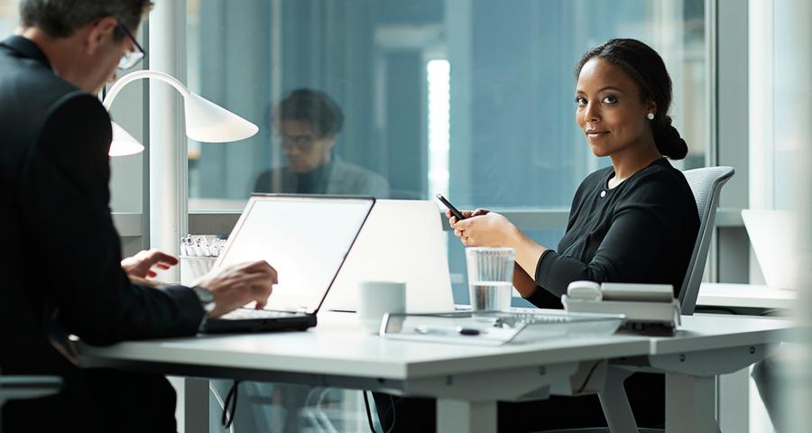 Business woman texting at a shared desk while look at the camera.