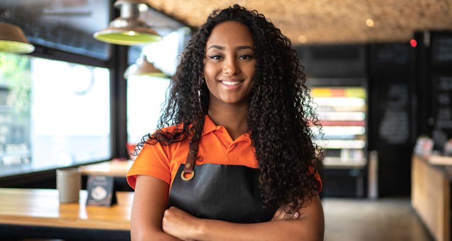 Young woman in a coffee shop smiling for the camera with her arms folded