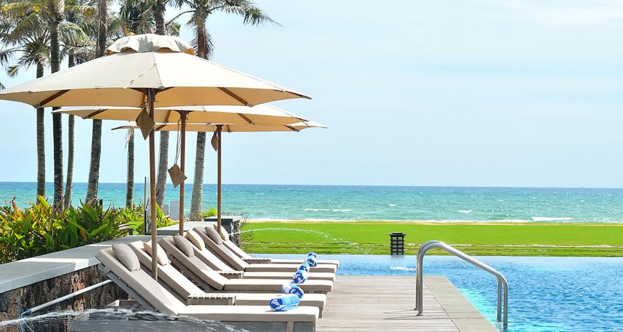 View of lounge chairs in the sun by an empty pool