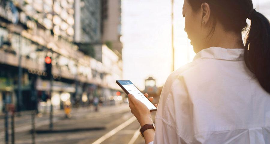 Woman looking at a cell phone while standing on a sidewalk