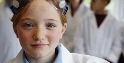 Young girl in a lab coat and googles smirking at the camera