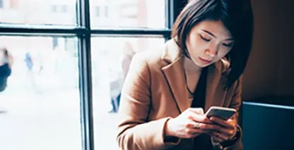 Woman looking down at her phone while sitting next to a window.