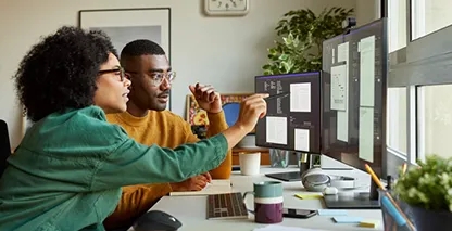 Man and woman sitting at a desk looking at documents on a computer. 