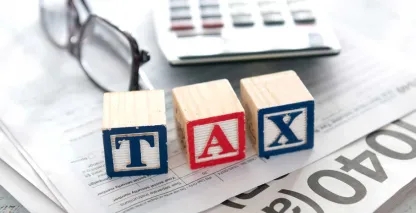 Tax documents on a desk and three letter blocks that spell T-A-X. 