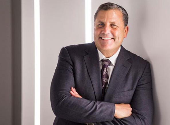 Smiling man in a suit leaning against a wall with his arms crossed