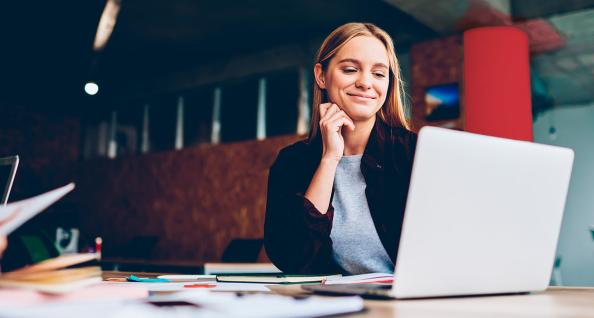 Woman in a black blazer looking at a laptop and smiling