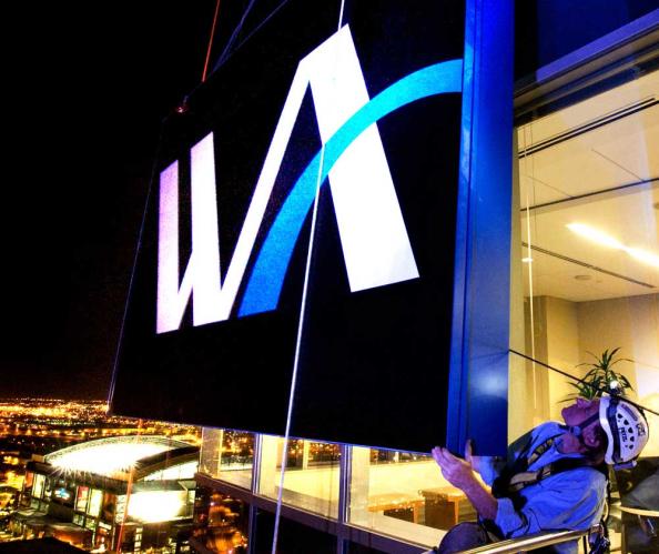 Two men hanging a large sign at the top of a skyscraper