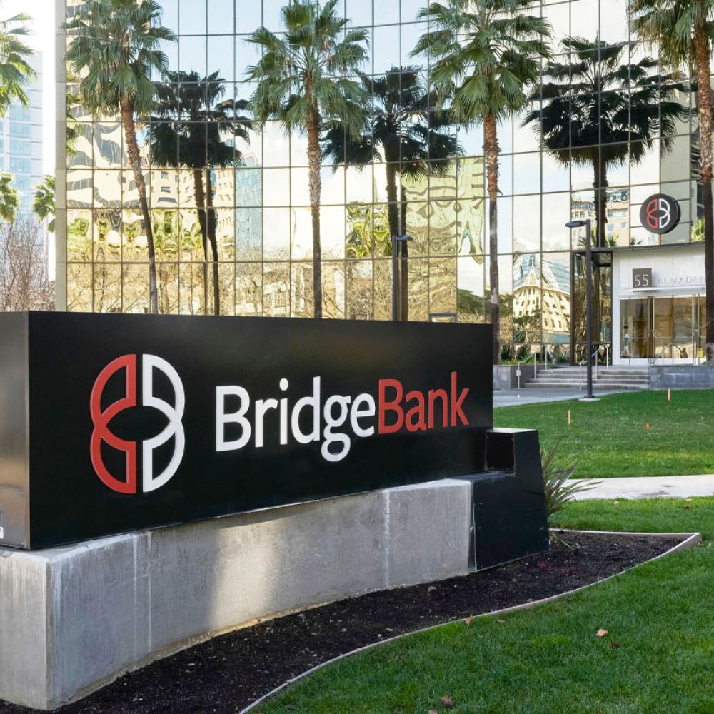 A grass lawn and glass building with the Bridge Bank sign out front