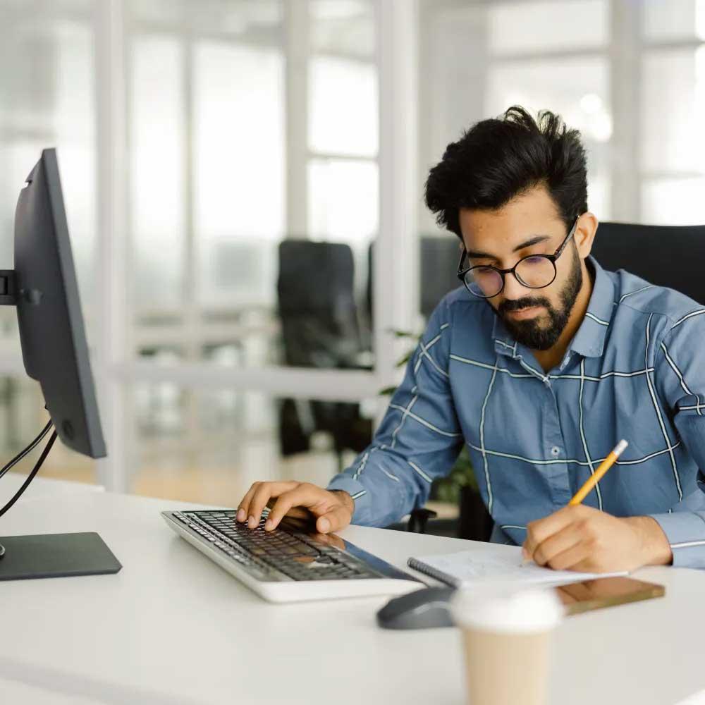 A young man working dilligently at a computer desk. He respresents the peace of mind gained from Positive Pay protections.