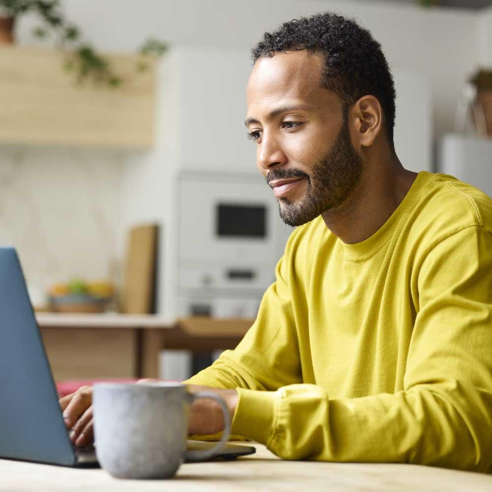 A man in his kitchen banking on a laptop. 